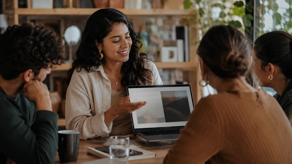 Equipo reunido alrededor de una mesa revisando una laptop junto a una facilitadora